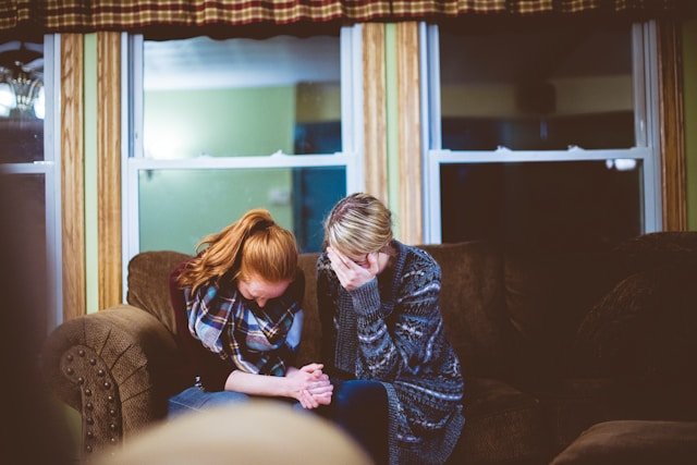 a mother and daughter crying on a couch processing grief after the LA wildfires