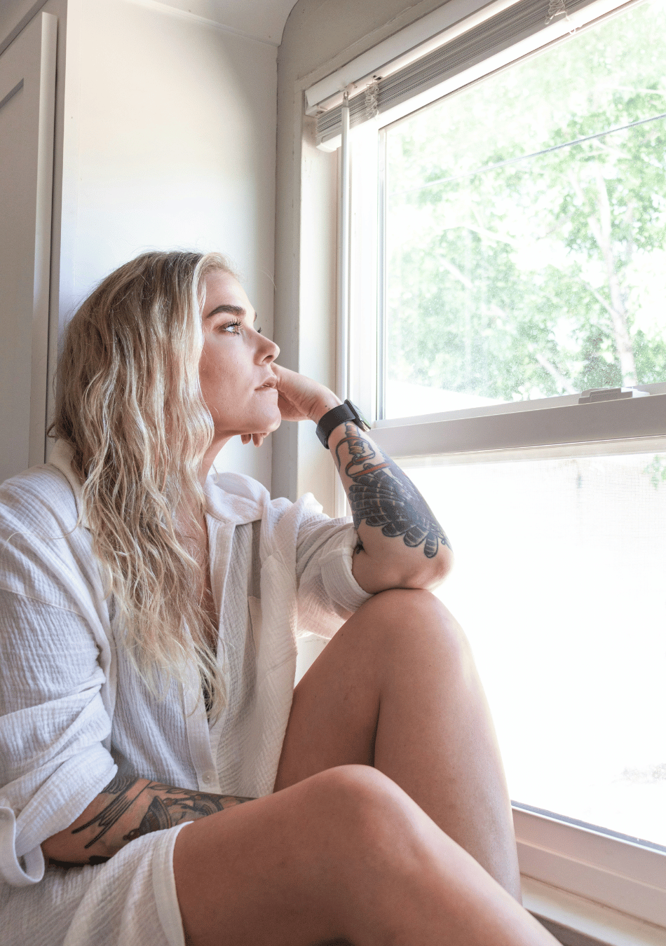 how to manage a mid-life crisis at thirty illustrated by a woman with blonde hair and an arm tattoo staring out the window with a sad expression
