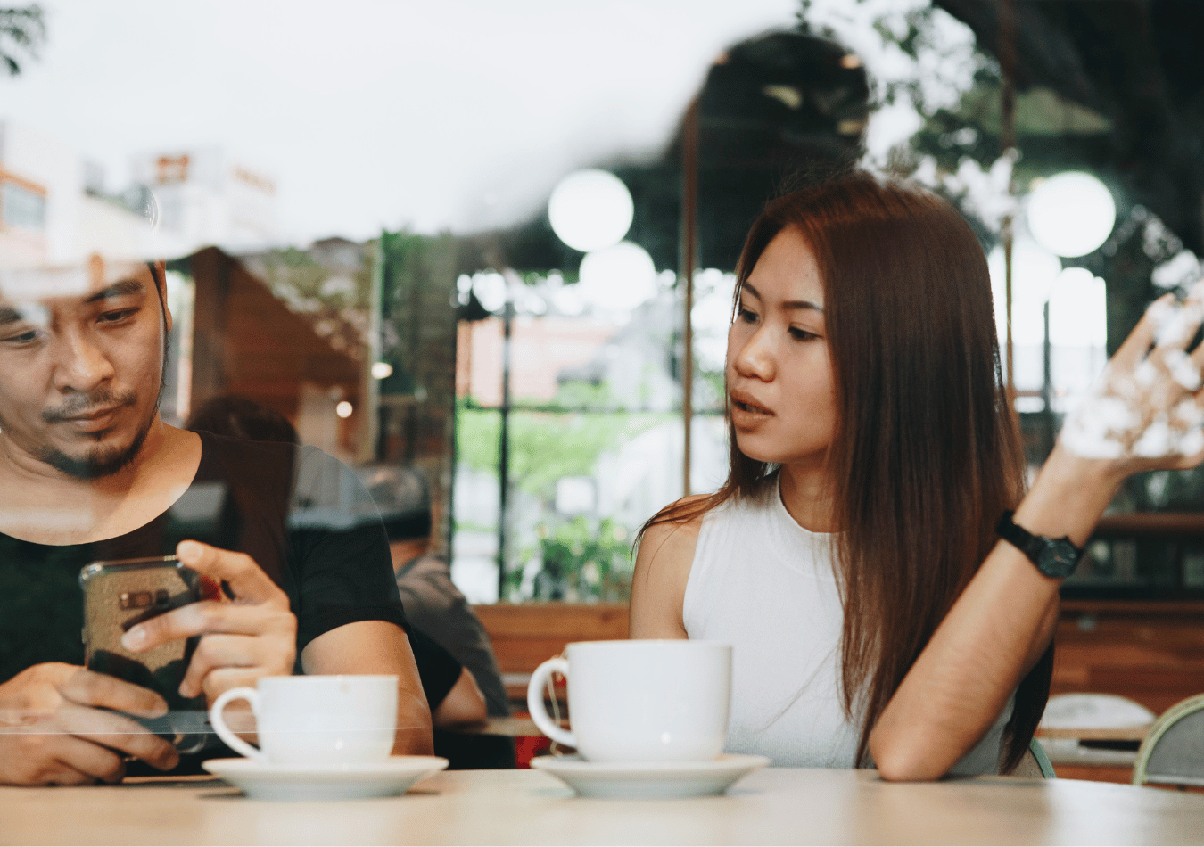 anxious-avoidant relationship advice from a therapist illustrated by an Asian couple talking in a coffee shop while one partner is distracted on his phone