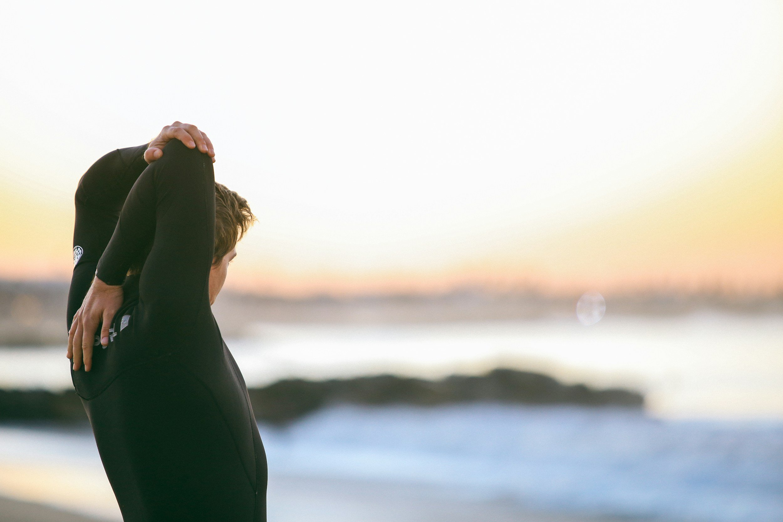 physical symptoms of trauma, a man stretching his upper back to stretch out his back pain looking at the water