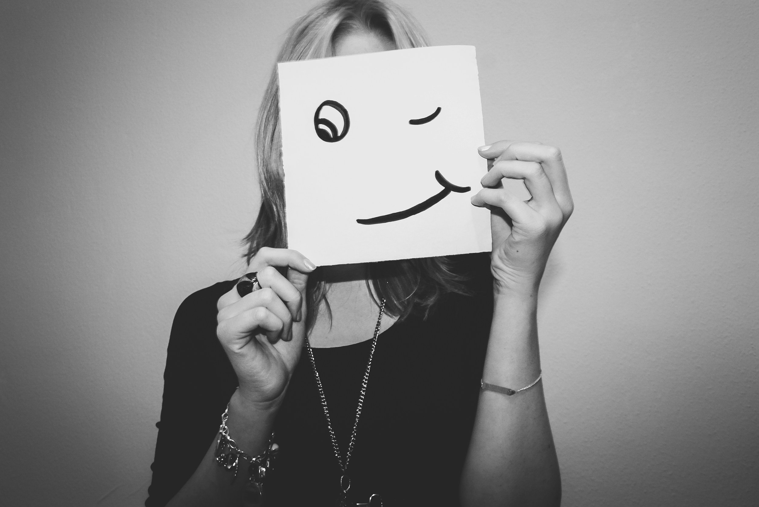 a woman holding a smile mask in front of her face to illustrate how people pleasing can often be a trauma response